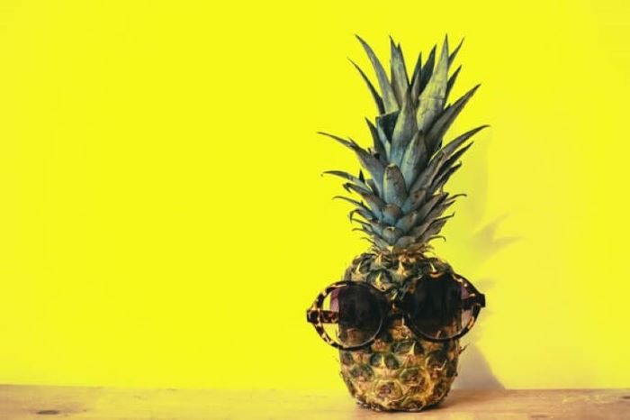 Pineapple wearing sunglasses set against a yellow background