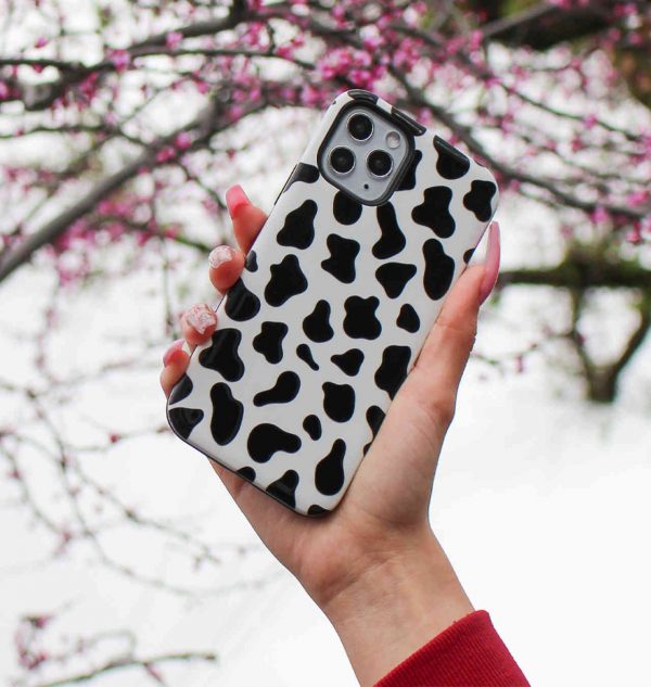 Hand holding a phone case with black and white cow design