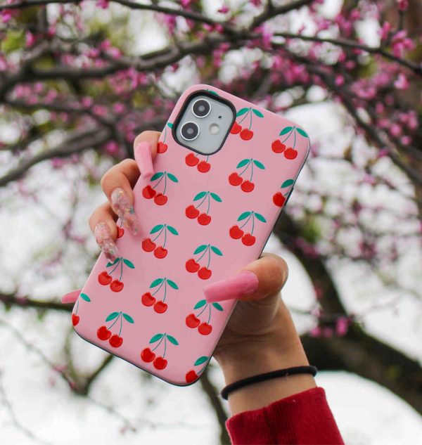 Hand holding a pink phone case decorated with red cherries
