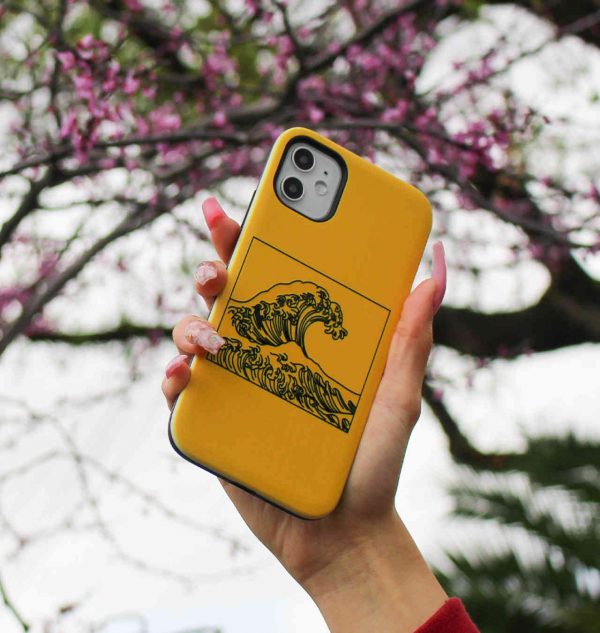 Hand holding a yellow phone case with a wave printed on the front
